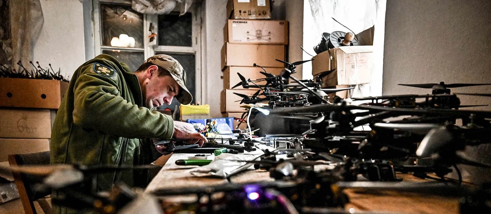 A soldier assembling FPV drones at a workbench crowded with airframes